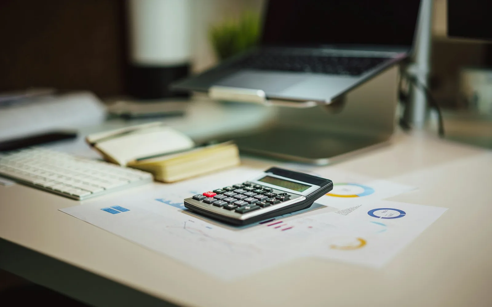 A calculator and financial charts beside a computer.